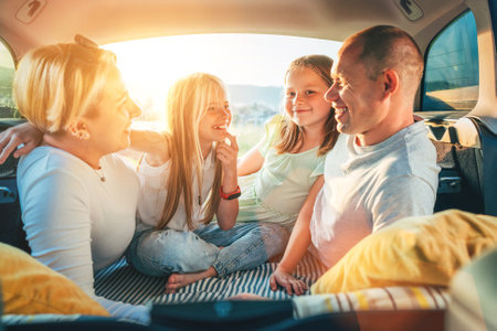 Portrait of happy smiling little sisters. Happy young couple with two daughters inside the car trunk during auto trop. They are smiling, laughing and chatting. Family values, traveling concept.の写真素材