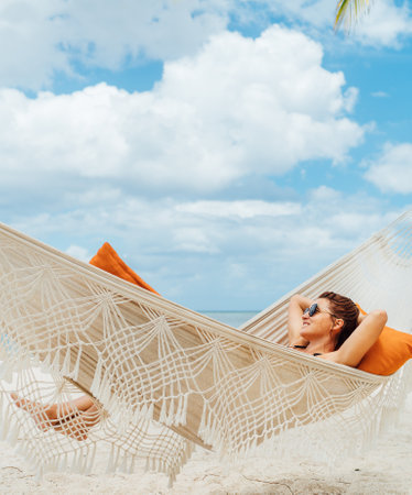 Young woman relaxing in wicker hammock on the sandy beach on Mauritius coast and enjoying wide ocean view waves. Exotic countries vacation and mental health concept image.の写真素材