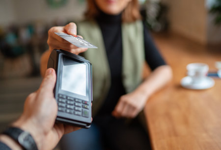 Young woman holding credit doing wireless bank payment with POS terminal process acquire at table in coffee shop cafe restaurant indoor. Focus on machine. Finance, restaurant industry, small business.の写真素材