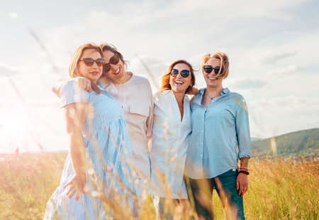 Portrait of four cheerful smiling and laughing women embracing during outdoor walking by high green grass hill. They looking at the camera. Woman friendship, relations, and happiness concept image.の写真素材