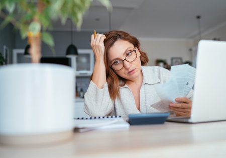 Beautiful middle-aged pensive woman in glasses with monthly bills thinking about family home budget. Small business, home finances, money savings concept image.の写真素材