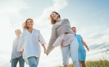 Portrait of four cheerful smiling women holding hand in hand walking by a high green grass meadow. They looking at the camera. Woman's friendship, relations, and happiness concept image.の写真素材