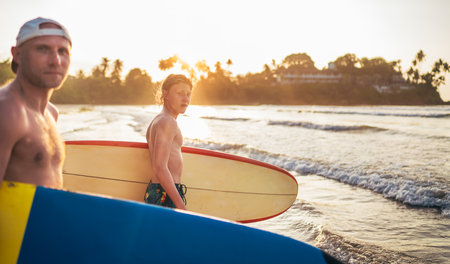 Teen boy with a surfboard goes to the sea surfing. He has a winter vacation and enjoying a beautiful...