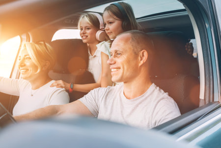 Happy smiling young couple with two daughters inside car during auto trop. They are smiling, and laughing during a road trip. Family values, tatraveling, automotive industry concept.の写真素材