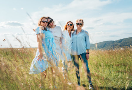 Portrait of four cheerful smiling women holding hand in hand walking by a high green grass meadow. They looking at the camera. Woman's friendship, relations, and happiness concept image.の写真素材