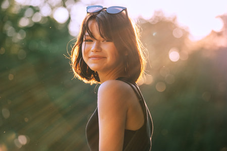 A beautiful young teenage girl dressed in a black dress cheerfully smiling at the camera with a warm sunset backlight. Beautiful people and a fashion concept image.の写真素材