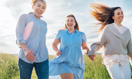 Portrait of three cheerful smiling women running by the meadow. Low angle photo shot on the blue sky with clouds. Woman's friendship, relations, and happiness concept image.の写真素材