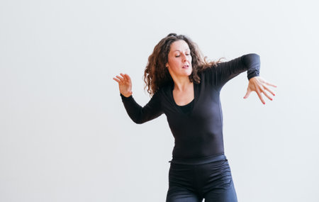 woman in black outfit laughs joyfully while dancing curly hair cascading over her shoulders. Expressive movements and radiant smile capture moment of pure happiness, freedom in minimalist settingの写真素材