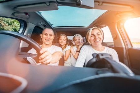 Happy young couple with two daughters inside car during auto trop. They are smiling, laughing during road trip. Family values, traveling concepts.の写真素材
