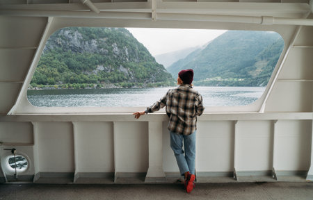 Woman enjoying fjord landscapes on Norwegian ferry with misty green mountains in background. Scene...