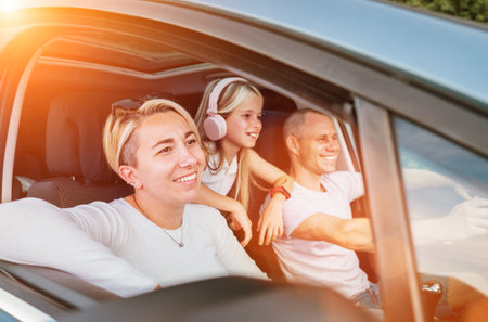 Cheerful young traditional family has a auto journey in modern car. Mother, father and daugher with headphones. Safety riding car and traveling concept image.の写真素材