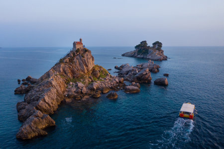 Aerial shot Sveta Nedjelja Island with magestic small church on cliff's top during evening sunset time hours with tourist boat, Balkans traveling, landmarks and Nature concept in Petrovac, Montenegroの写真素材