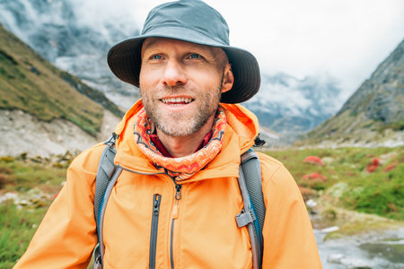 Portrait of smiling Man with backpack dressed orange waterproof jacket and funny hat walking the path during Makalu Barun National Park trek in Nepal. Mountain hiking and active people concept image.の写真素材
