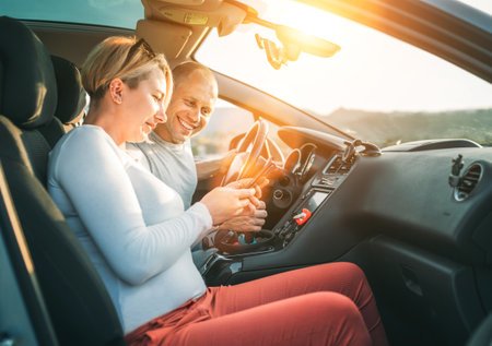 Happy smiling two young adulds couple using smartphone navigation inside car during auto jorney.They are laughing during road trip. Family, couples relations values, car sharing and traveling conceptsの写真素材
