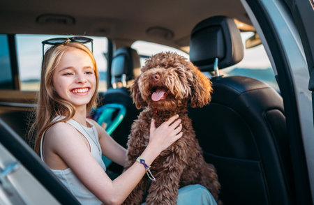 Portrait of a brown Maltipoo dog with a smiling little girl while they sit in the back seat during a car journey. Funny pets in a modern family concept.の写真素材