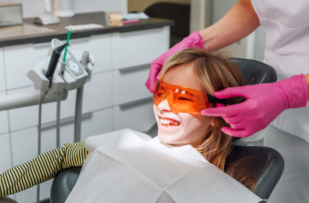 Dentist doctor wearing protective eyeglasses to little girl during teeth restoration, dental fillings procedure with curing UV light. Health care, teeth beauty and medicare industry concept image,の写真素材