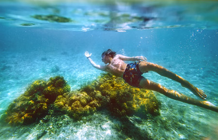 Diving teenage boy snorkeling over the coral reefs underwater photo in the clean turquoise lagoon on Le Morne palm trees beach with Le Morne Brabant mount. Mauritius island. Exotic traveling conceptの写真素材