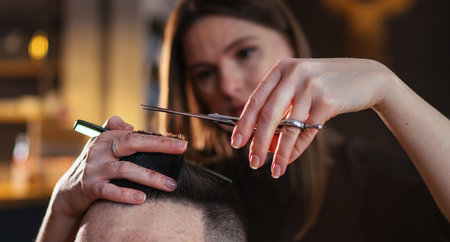 Young hairdresser female hands with scissors and comb hairstyle hairdressing close-up image in modern low light black style barber shop. Haircare service small business Cosmetics and personal careの写真素材