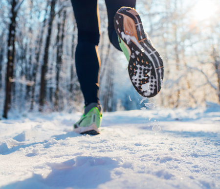 Running shoes sole close up image of winter jogger feet in running sneakers on the snowy park path during sunny day. Rear view sole shot.の写真素材