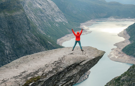 Woman trekker dressed bright red jacket enjoying glacier Ringedalsvatnet lake jumping rose arms UP...