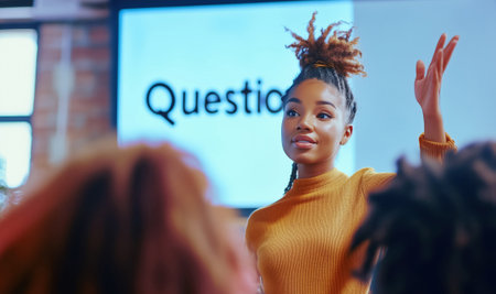 Image shows small group discussion in modern indoor space. Focus on participant with dreadlocks, raising hand for question. Screen in background reads "Questions". Teamwork, discussion and brainstormの素材