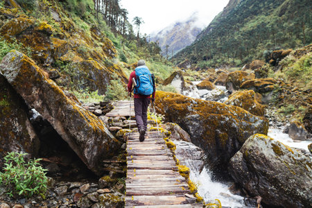 Man with backpack and trekking poles crossing mountain creek wooden bridge during Makalu Barun National Park trek in Nepal. Mountain hiking and active people concept image.の写真素材