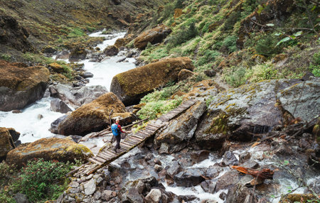Man with backpack and trekking poles crossing mountain creek wooden bridge during Makalu Barun National Park trek in Nepal. Mountain hiking and active people concept image.の写真素材