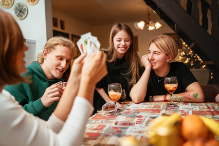 Cheerfully warm home togetherness cozy scene of family playing cards together in home kitchen. Girls and boys smiling and laughing with moms. Holidays time spending and relations concept image.の写真素材