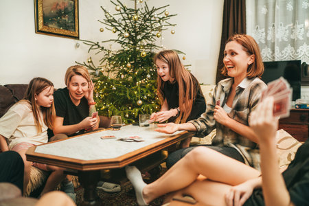 Cheerfully warm home togetherness cozy scene of family playing cards together in home livingroom. Girls smiling and laughing with moms next Christmas tree. Holidays time spending relations conceptの写真素材