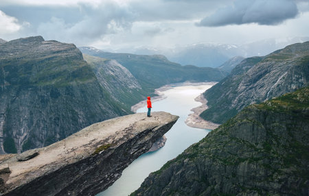 Woman trekker dressed bright red jacket enjoying glacier Ringedalsvatnet lake from famous Trolltunga "Troll's Tongue" cliff. Trolltunga trek final point in Norway.の写真素材