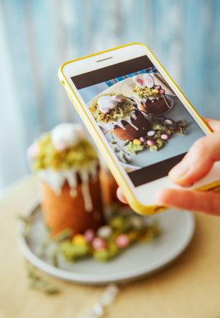 Food bloger making photo using modern smartphone. Paska - the Easter Eve sweet bread with icing decorated with eatable "moss" still life. Popular dessert during Eastern Orthodox Easter Holidayの写真素材