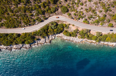 Aerial vertical shot of pickup cars moving by the curved road near sea tranquil waves on coast on Cephalonia Greek island. Transportation, traveling and nature concept.の写真素材