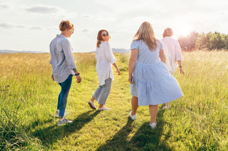 Portrait of four cheerful smiling women holding hand in hand walking by a high green grass meadow. They looking at the camera. Woman's friendship, relations, and happiness concept image.の写真素材