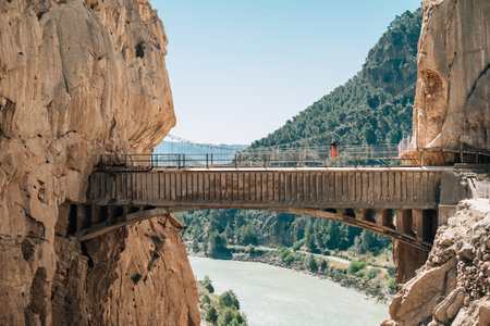 Lonely hiker woman standing on Hanging Bridge over the mountain river and enjoying Spanish Malaga province valey landscape during Caminito del Rey hiking tour in narrow Canyon. South Spain.の写真素材