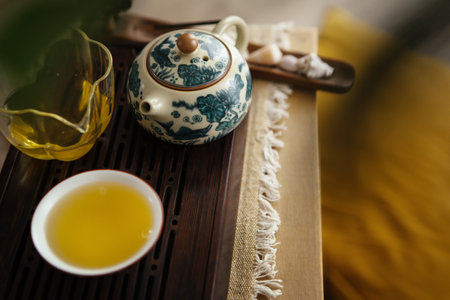 Still life photo of patterned clay teapot, clear glass pitcher, tea cup with fresh brewed green oolong tea. Soft light, wooden tea tray evoke calming mindful ceremony atmosphere.の写真素材