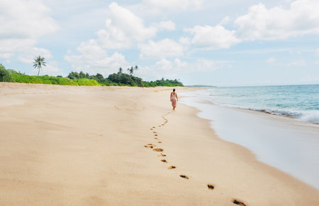 Young female dressed in light summer clothes walking barefoot leaving footprints on the sand on Indian ocean Tangalle lonely coconut trees beach on Sri Lanka island. Aerial top view drone shot.の写真素材
