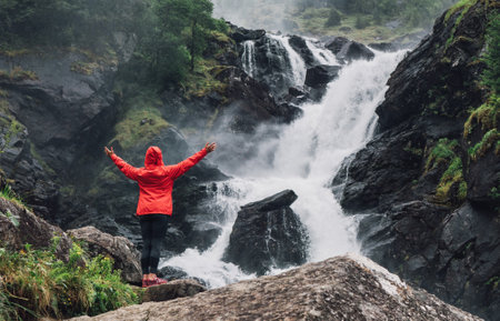 Woman trekker dressed bright red waterproof jacket at LÃ¥tefossen Waterfall, Norway