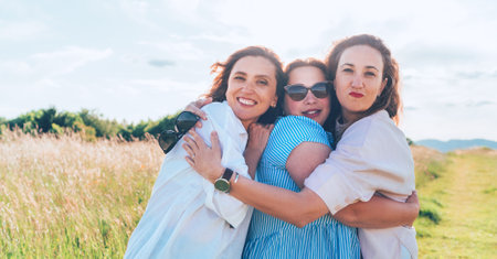 Portrait of three cheerful smiling women embracing during outdoor walking. They looking at the camera. Woman friendship, relations, and happiness concept image.の写真素材
