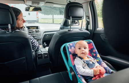 Portrait of laughing baby in car seat while Mother driving a passenger car. Scene captures moment of care and responsibility, highlighting importance of child safety during auto trip travel.の写真素材