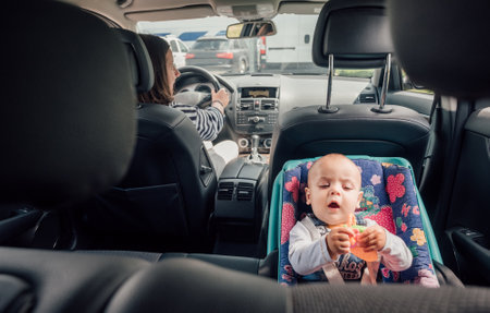 Portrait of laughing baby in car seat while Mother driving a passenger car. Scene captures moment of care and responsibility, highlighting importance of child safety during auto trip travel.の写真素材