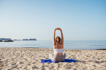 Calm woman sitting and doing deep breathing and stratching exercises and meditating in early morning hours on sandy beach with calm sea waves. Mental health, people relaxing, traveling concept.の写真素材