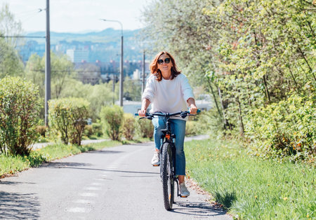 Cheerfully smiling Caucasian woman in fancy sunglasses riding a bicycle on the city park street. Ecology sustainable transport and happy people concept image.の写真素材