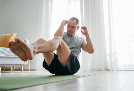 Young muscular man performing bicycle abs exercise on living room floor. Healthy lifestyle or sporty people concept image.Core workouts like this boost fitness and support overall health.の写真素材