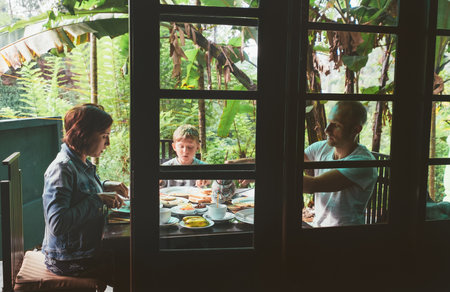 Family enjoying outdoor breakfast in tropical jungle setting surrounded by lush greenery and banana...
