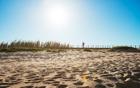 Lonely backpacker man walking by sandy Portugese beach in morning. Path leading by wooden passadicos  - boardwalks along the ocean coast. Shot during the Camino Portuguese â  popular pilgrimage routeの写真素材