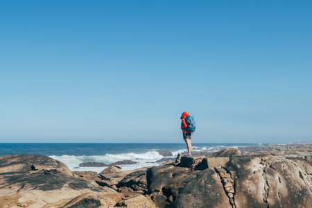 Beautiful short of female backpacker on Atlantic ocean rocky coast in Spain. Shot during the Camino Portuguese â  popular pilgrimage route. Beauty in Nature concept.の写真素材