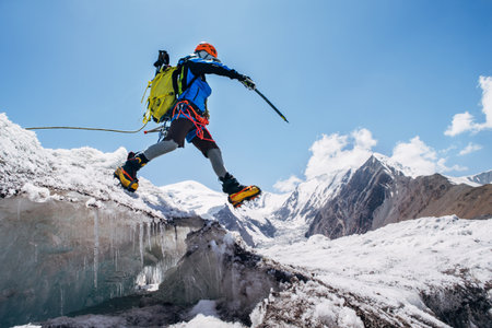 Climber in vibrant gear leaps over crevasse on icy glacier during Lenin peak ascent under clear sky...