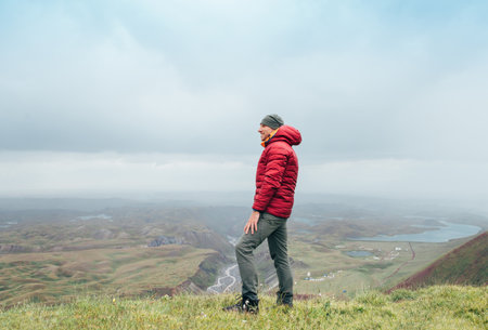 Smiling middle-aged man dressed down jacket enjoying Tulpar-Kol lake landscape during Pamir mountains trekking. Lenin peak climbing acclimatization route near 3600m Base Camp, Kyrgyzstan, Central Asiaの写真素材