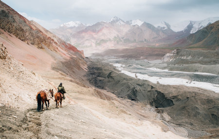 Beautiful picturesque wide angle Pamir mountains valley shot with horsemen heading by dusty mountain...