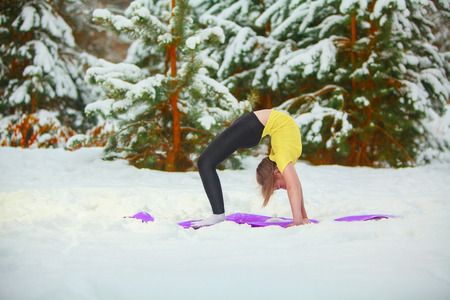 beautiful woman doing yoga outdoors in the snow in yellow T-shirtの写真素材